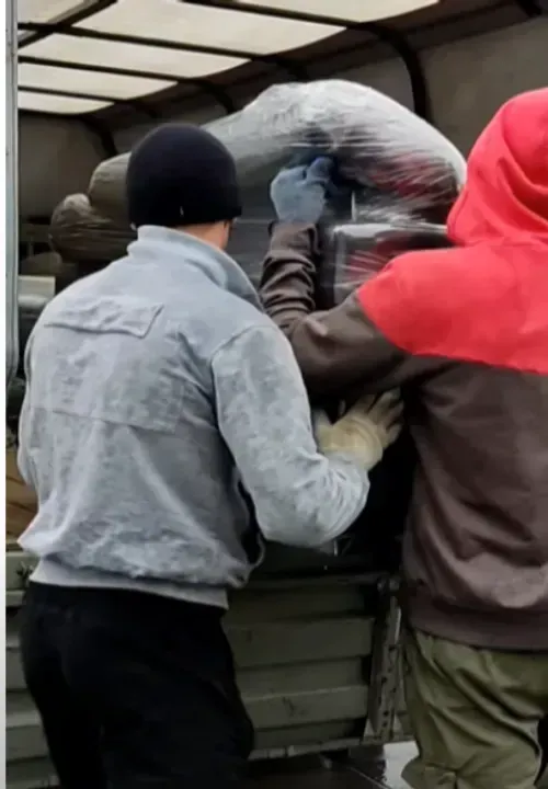 Two movers loading wrapped furniture into the truck