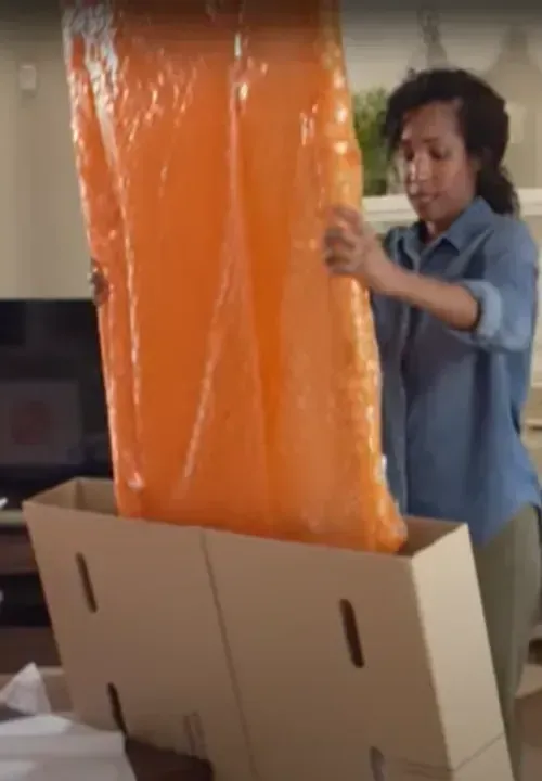 Packer sliding a wrapped item into a moving box