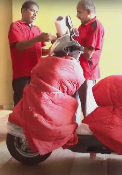 Two movers wrapping a scooter in red protective covers